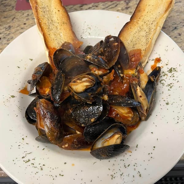 Steamed mussels in red sauce with two slices of toasted bread on a white plate.