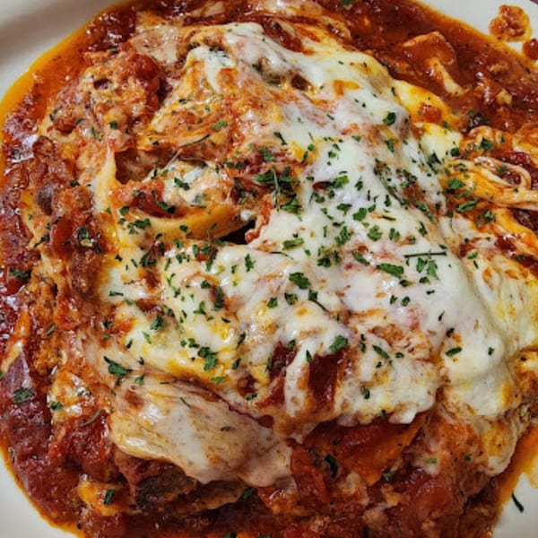Close-up of baked ziti or lasagna with melted cheese, red sauce, and parsley on a white plate.