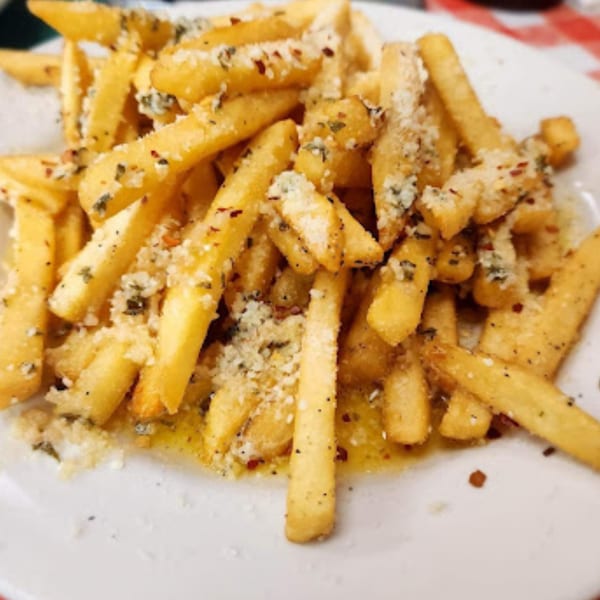 Golden french fries topped with grated cheese, herbs, and spices on a white plate.