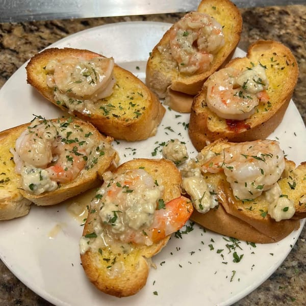 Garlic bread slices topped with creamy shrimp and parsley on a white plate.